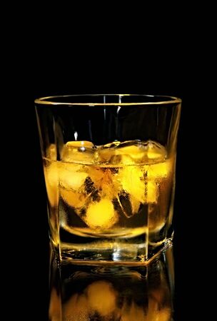 Scotch whiskey on ice, with black background, on reflective surface.の写真素材