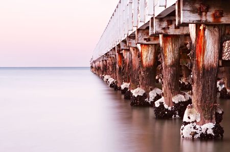 Pier in dawn light, over calm ocean.  A tranquil scene, with weathered old pylons, rusted bolts and barnacles.の写真素材