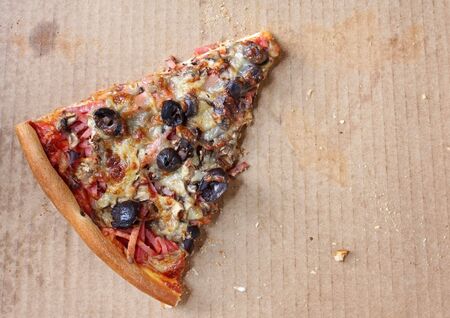 Last lonely slice of pizza, in pizza box.  Capricciosa, with black olives, ham, mushrooms,  and mozzarella.の写真素材