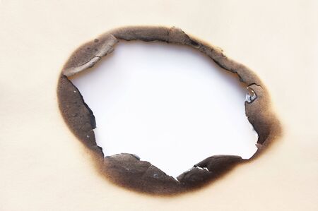 Burn hole in cardboard, casting shadow on white beneath.の写真素材