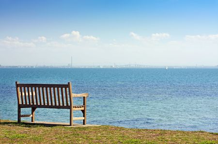 Empty park bench overlooking the ocean, on a bright sunny day.の写真素材