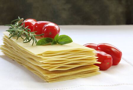 Lasagne sheets ready for cooking, with  roma tomatoes, and fresh basil and rosemary.の写真素材