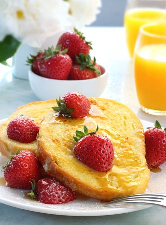 French toast with fresh strawberries, maple syrup and powdered sugar, and orange juice behind.  A...