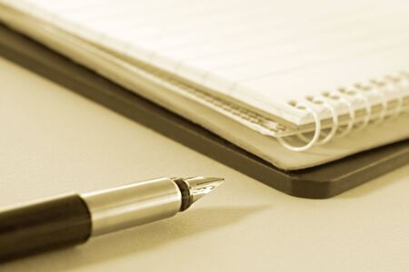 Fountain pen with notepads.  Focus on tip of pen, sepia tone.