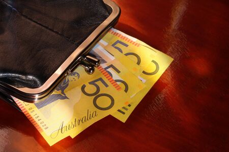 Coin Purse with Australian fifty dollar notes.  Against polished timber, in mottled natural light.の写真素材