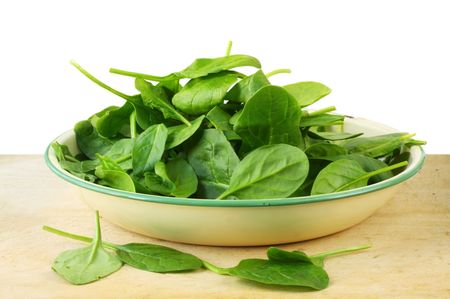 Old enamel bowl full of  spinach leaves, on old chopping board.