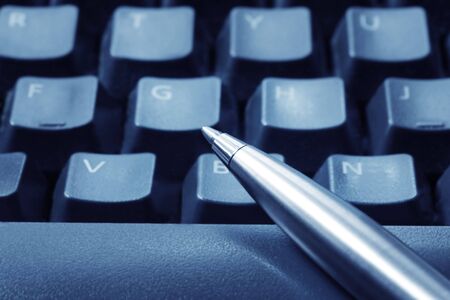 Ballpoint pen resting on computer keyboard.  Blue tone, focus on pen tip.の写真素材