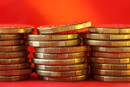 Stacks of golden coins, over red background with warm light.の写真素材