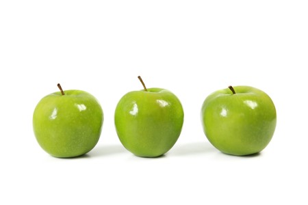 Three green apples in a row, casting natural shadow on white.の写真素材