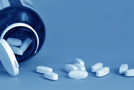 Pills spilling from a bottle.  Blue toned image, with lots of copy space.