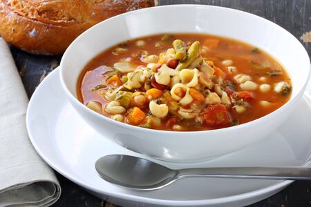 Bowl of minestrone pasta soup, on rustic table, with cob of tomato bread.の写真素材