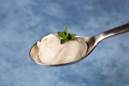 A spoonful of mayonnaise with herbs, over blurred blue background.の写真素材