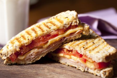 Grilled sandwich with ham, cheese and tomato, and a glass of milk behind.の写真素材