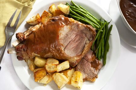 Roast leg of lamb on a serving platter, with potatoes, beans, and gravy.の写真素材