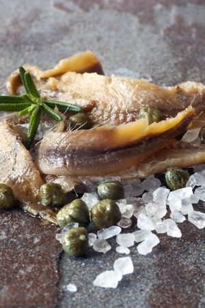 Anchovy fillets with baby capers, sea salt, and rosemary, over rough stone.の写真素材