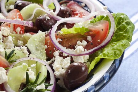 Close-up of bowl of Greek salad.  Luscious vine-ripened tomatoes, with feta cheese, kalamata olives, cucumber, red onion, kos lettuce and rosemary.の写真素材
