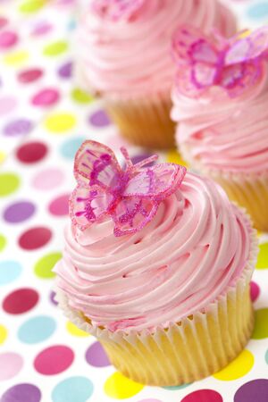 Vanilla cupcakes with pink frosting and glittery butterflies, over polka dot background.  Fun!の写真素材