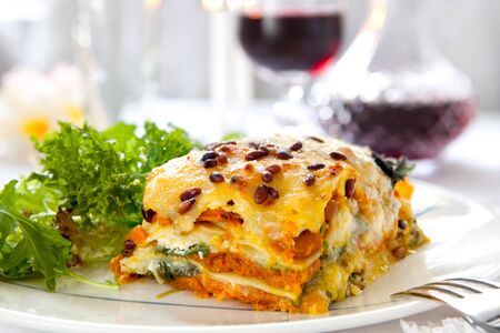 Vegetarian lasagne topped with toasted pine nuts and melting cheeses.  With salad and red wine.の写真素材