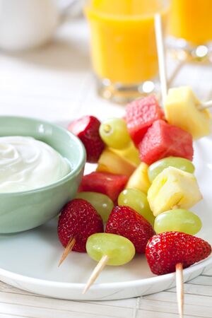 Platter of fruit skewers with a dish of yogurt.  Healthy party food, with orange juice behind.の写真素材