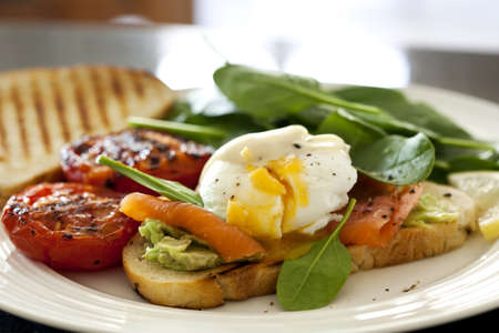 Poached egg on toast, with smoked salmon, avocado, grilled tomato, and baby spinach.の写真素材
