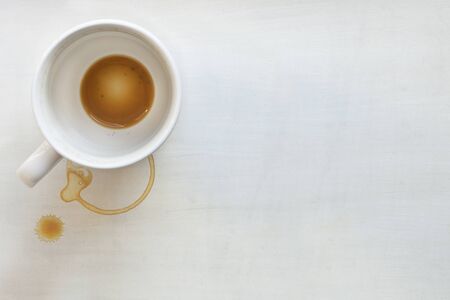 Coffee cup over white painted background.  Dregs in the bottom of the cup, with stains.  Lots of...