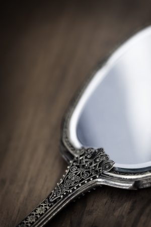 Antique gilded hand mirror, over dark timber.  Soft focus.の写真素材