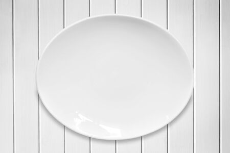 Empty white oval plate on white timber background.の写真素材
