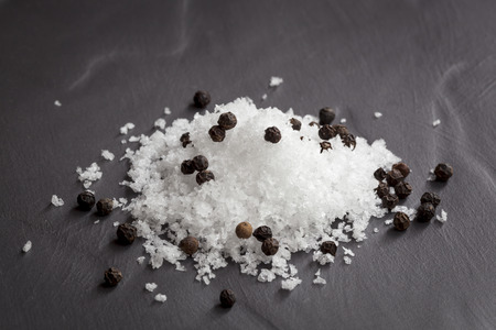 Sea salt flakes and black peppercorns over dark slate.の写真素材
