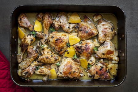 Roast chicken in roasting pan, with lemon, garlic and thyme.  Overhead view, on black slate.の写真素材