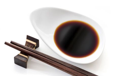 Dish of soy sauce with chopsticks, over white.の写真素材