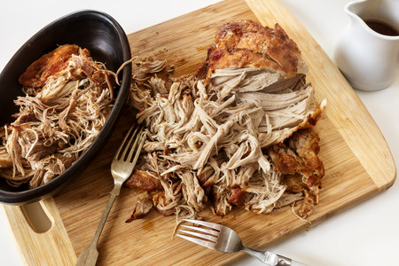 Pulled pork roast on board with forks and jus.  Delicious shredded meat.