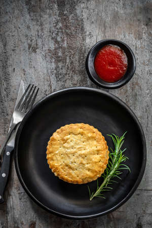 Meat pie on black plate over rustic timber.  With rosemary and tomato saucer or ketchup.の写真素材