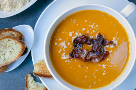Pumpkin soup with proscuitto ham, parmesan cheese and crusty bread.  Top view, in white bowl.の写真素材