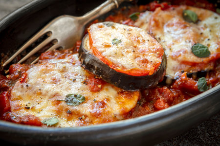 Baked eggplant or aubergine, with tomato and mozzarella, in black dish over slate.の写真素材