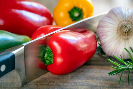 Food background with chefâs knife cutting red bell pepper or capsicum with garlic and herbs on wooden chopping boardの写真素材
