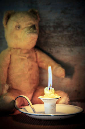 Vintage enamel candle holder with shabby old teddy bear behind.  Selective focus on candle holder.の写真素材
