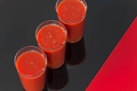 tomato juice on black-red glass background.
