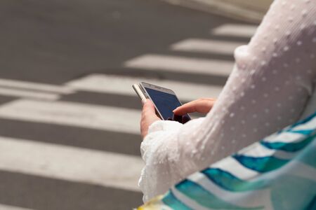 A woman at a pedestrian crossing looking at the smartphone. safety concept