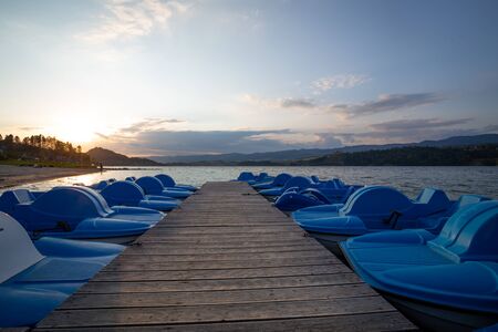 the sun setting over the water. A bridge with boats for rest and swimming on the lakeの写真素材