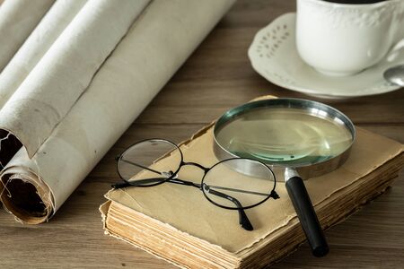 A book with old-fashioned glasses, a magnifying glass and rolled up old parchments
