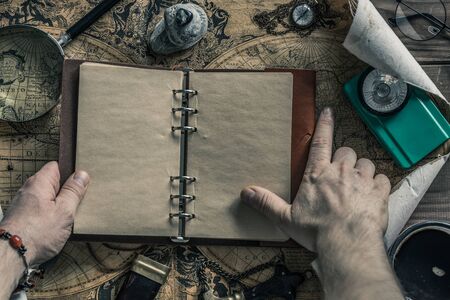 Travel planning around the world trip. A finger roaming the map. An open notebook with space for text. Things useful in the expedition. Retro style.の写真素材