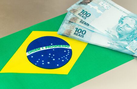 Brazilian money banknotes on the background of the flag of the country