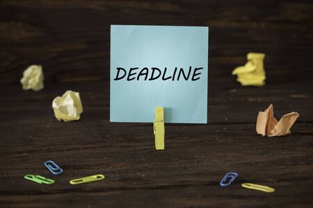 card attached to the clip with the handwritten inscription Deadline. Wooden background. Office and...