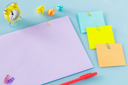 A yellow alarm clock, along with colorful, blank note cards. Top view. Colorful office staples,...