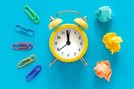 small yellow alarm clock on blue background, Colorful office staples and crumpled paper balls. Top...