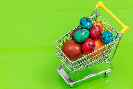 A shopping cart filled with Easter eggs. The concept of Holiday shopping and high prices. Green background, place for an inscriptionの写真素材