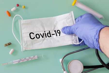 hand in a medical glove grabbing a protective mask with the inscription "Covid-19" medical instruments, thermometer, medicineの写真素材