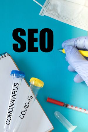 coronawirus vial, notebook, hand in a rubber glove with a pen and the inscription SEO. The concept of using the virus and fear of it for business purposesの写真素材
