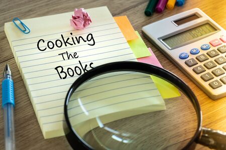 Notebook with the words "Cooking the books" Creative accounting concept. Calculator, office accessories, magnifying glassの写真素材