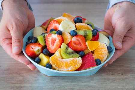 Fresh Fruit Salad, The man holds a plate full of sliced fruit over the tableの写真素材